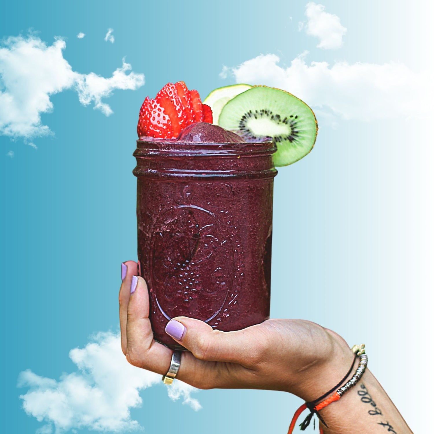 Hand holding a purple smoothie with fruit against a blue sky background