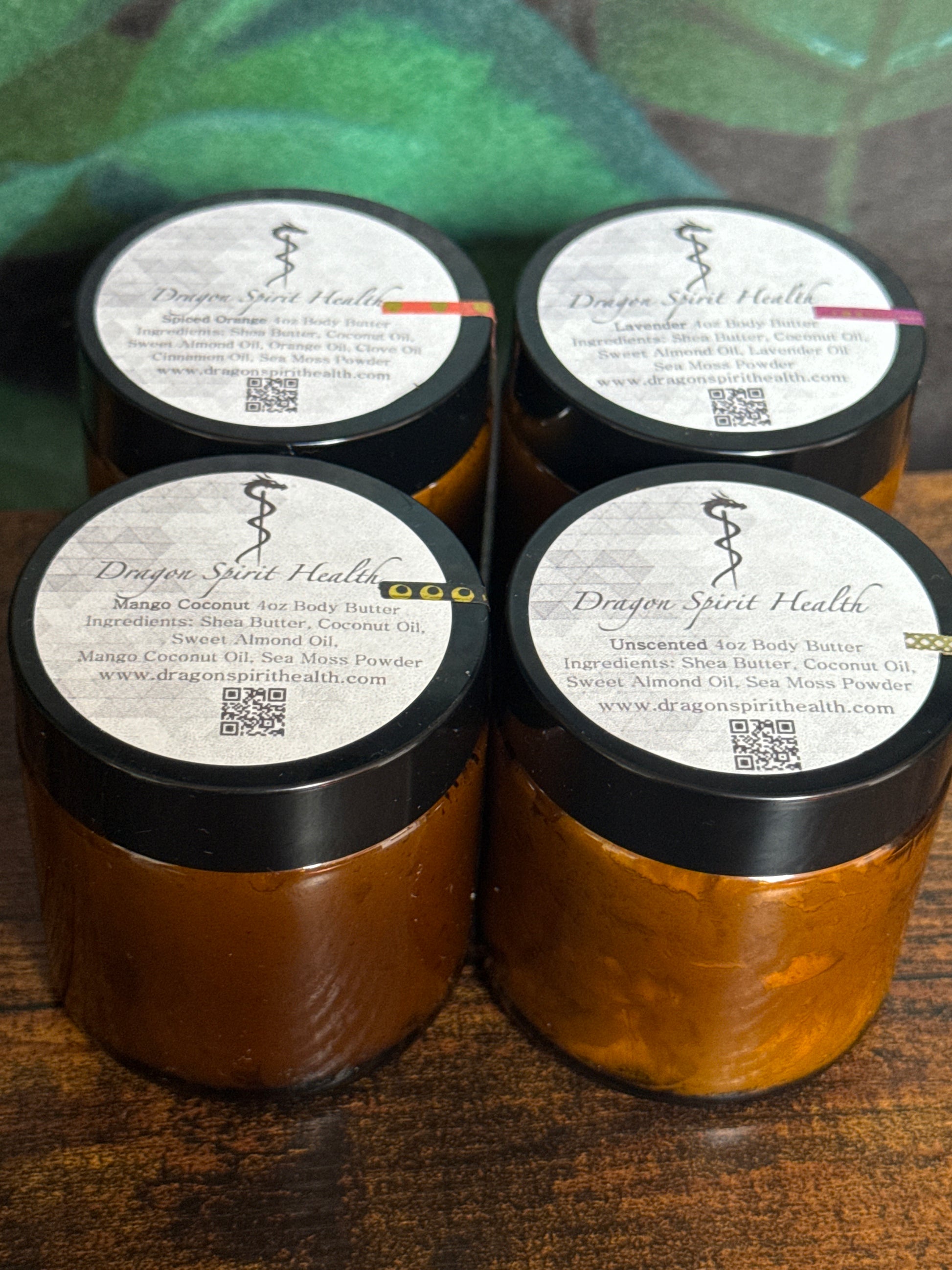 Four amber-colored jars of all natural sea moss body butter with black lids on a wooden surface